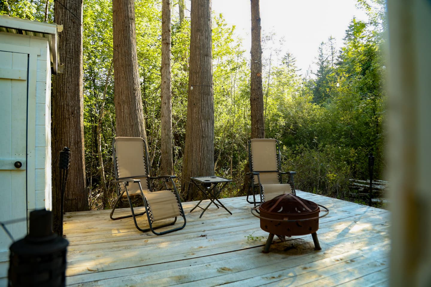 Two reclining chairs and a fire pit on the wooden deck among the trees